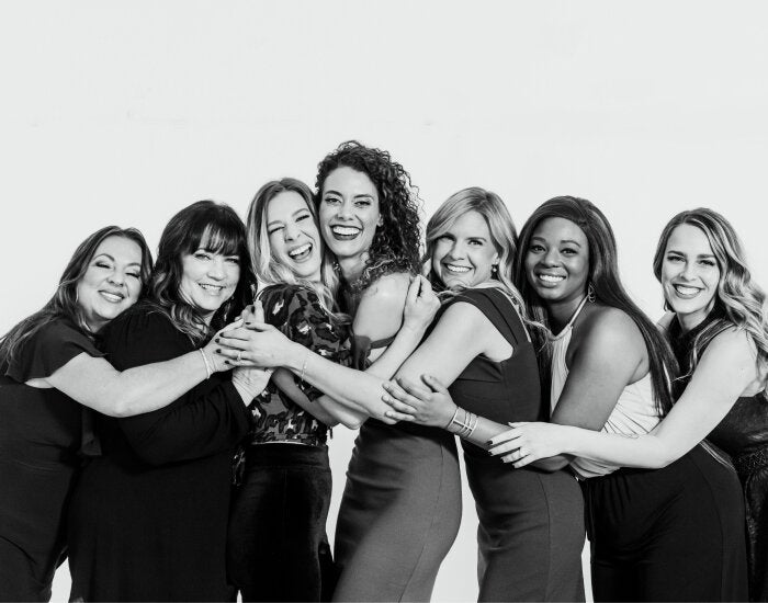 Group of women posing together with arms around each other on a white background